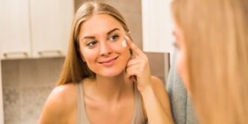 Jovem mulher na frente do espelho aplicando hidratante facial na pele oleosa.